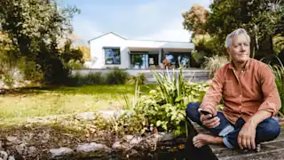 Mann mit Smartphone sitzt im Garten an einem Teich