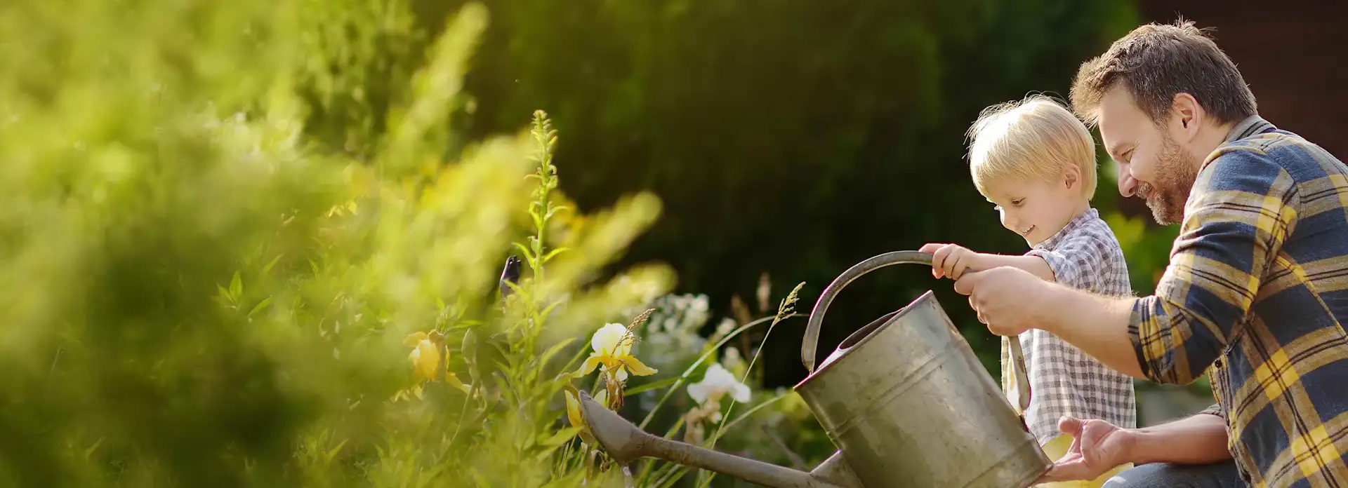 Vater und Sohn gießen im Frühling grünen Garten mit Gießkanne
