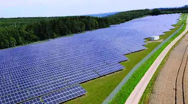 Solarpark mit Solarpanels auf der Wiese zwischen Feld und Wald