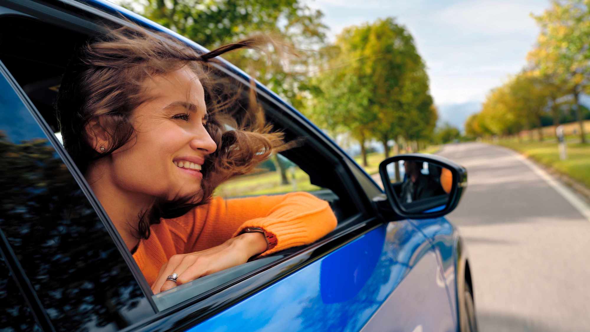 Lachende Frau schaut aus dem Fenster eines E-Autos.