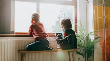 2 Kinder sitzen an der Heizung und schauen aus dem Fenster.