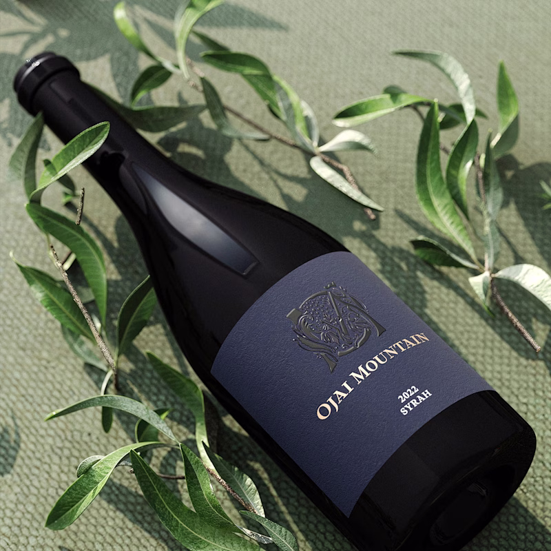 Ojai Mountain 2022 Syrah bottle lying among scattered olive leaves