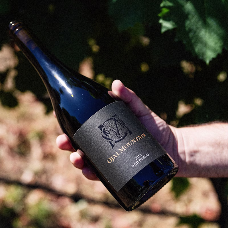 Hand holding Ojai Mountain 2021 Red Blend bottle in the vineyard