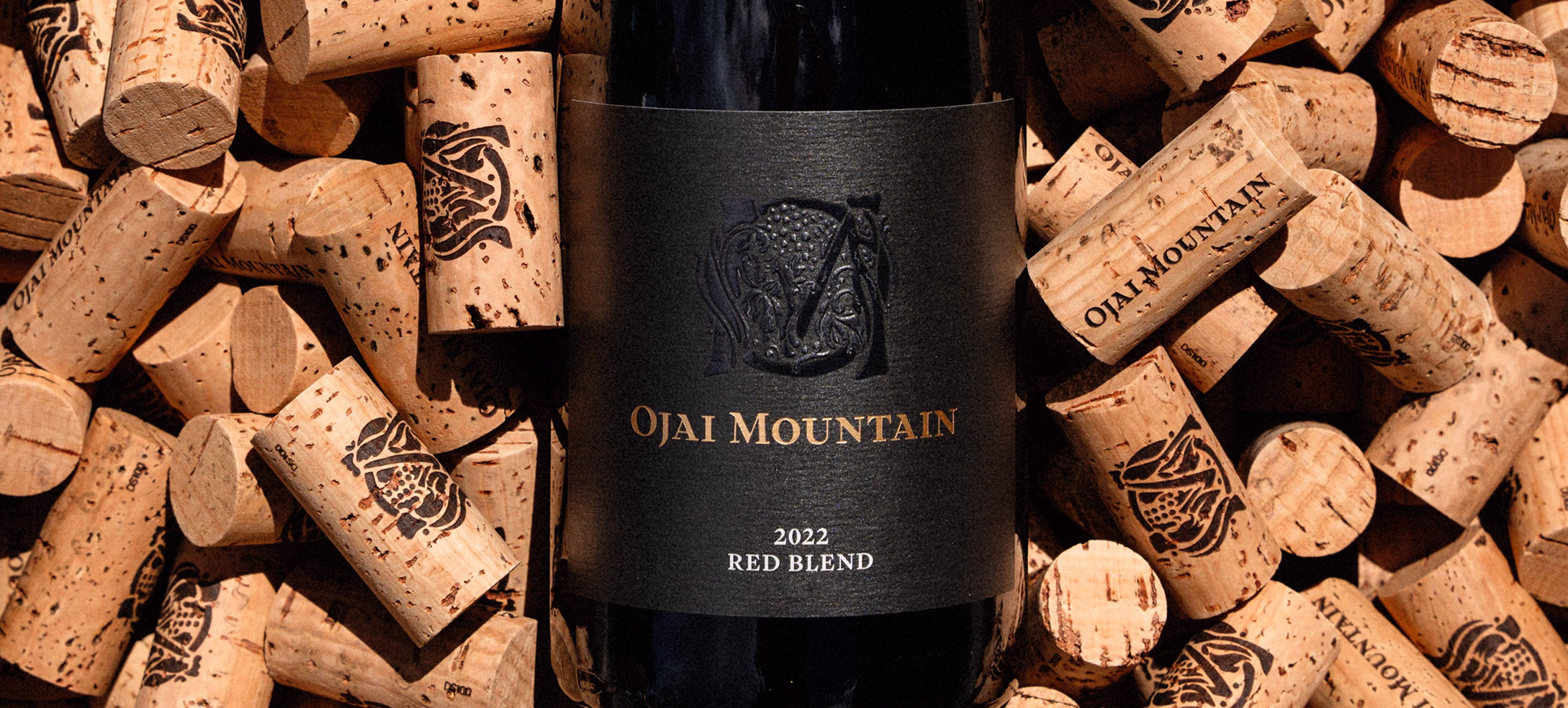 Ojai Mountain 2022 Red Blend bottle surrounded by branded corks Ojai Mountain 2022 Red Blend bottle surrounded by branded corks