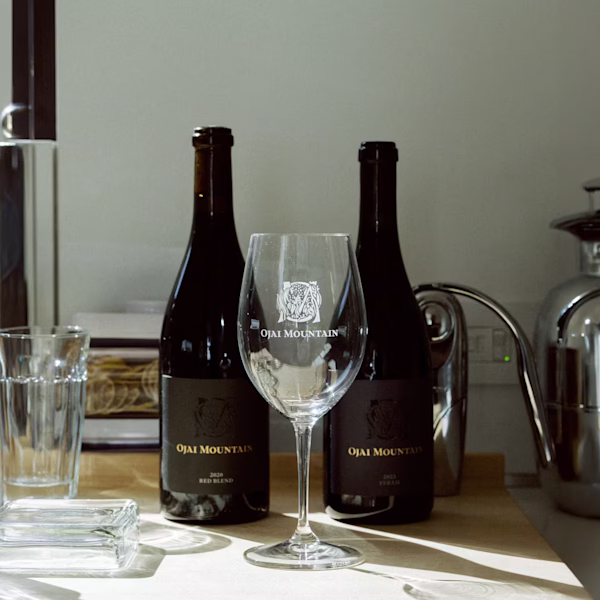 Ojai Mountain Wines Against the Mountain Backdrop Two Ojai Mountain wine bottles and a glass on a table with mountain landscape beyond