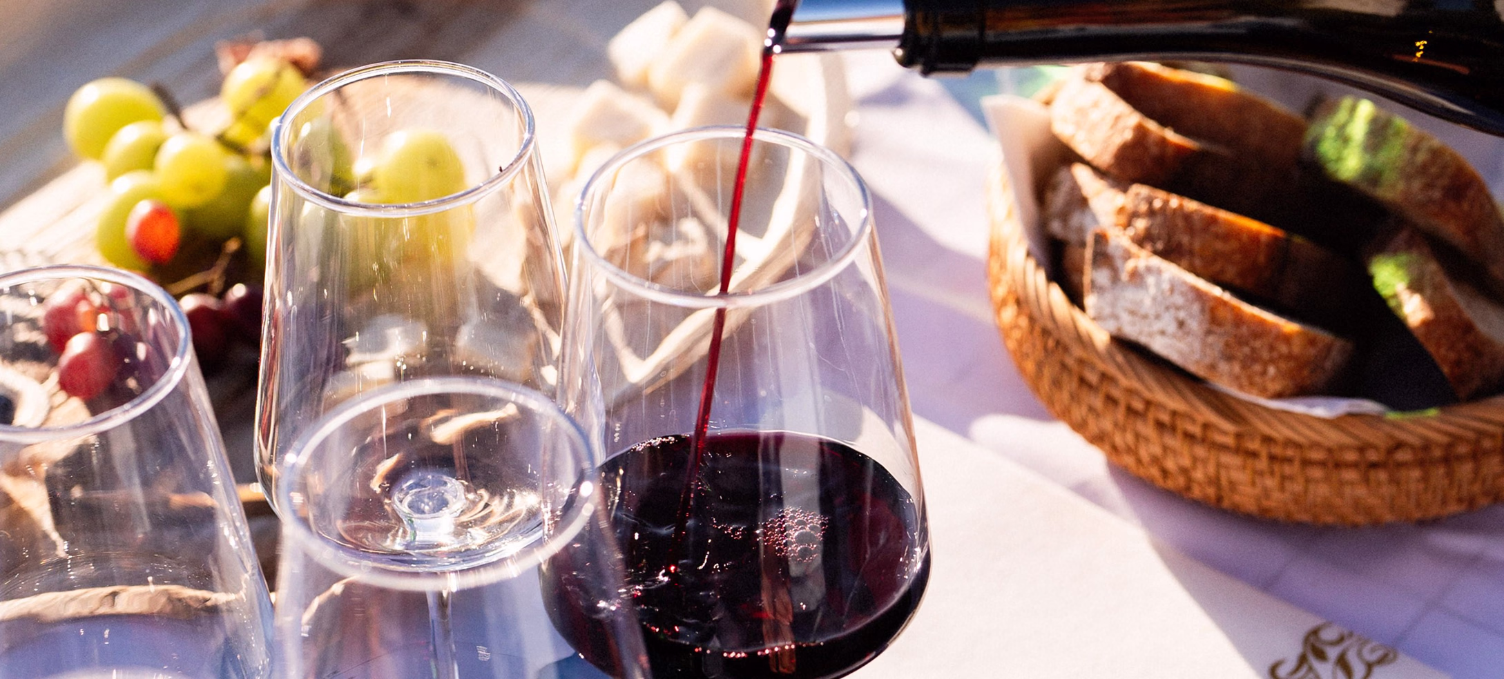 Red wine poured into glasses on a table with bread and grapes