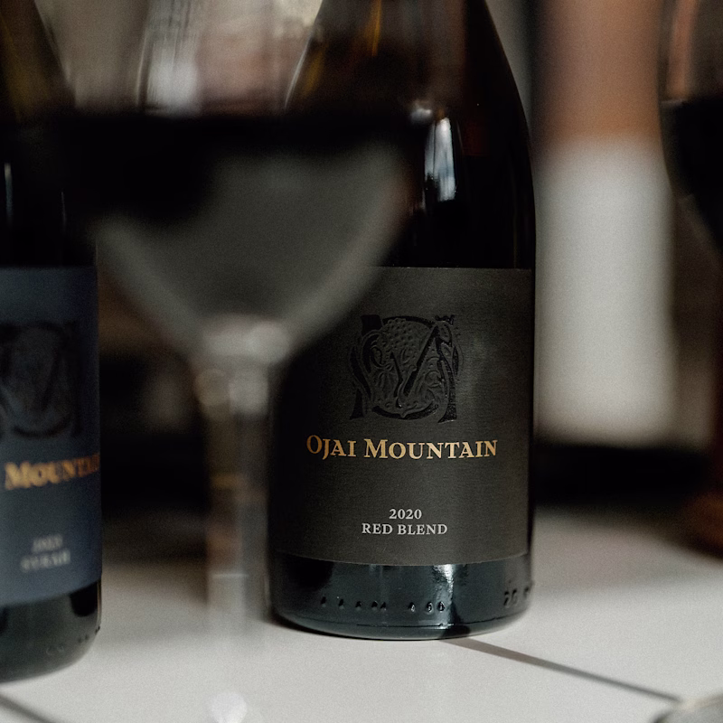 Two Ojai Mountain 2020 Red Blend bottles with a glass in soft light