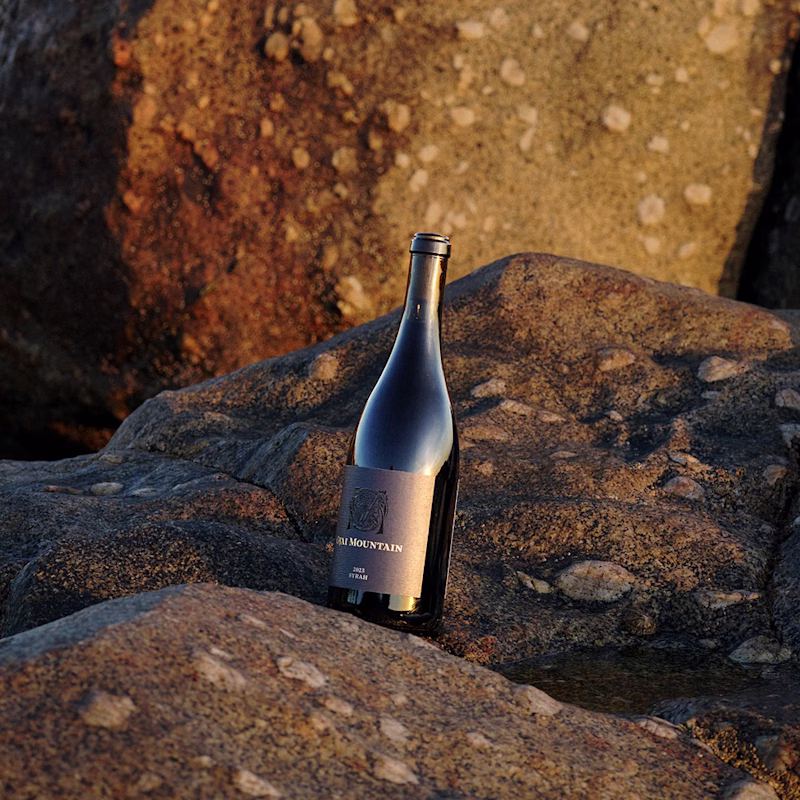 Ojai Mountain 2023 Syrah bottle resting on wet dark rock