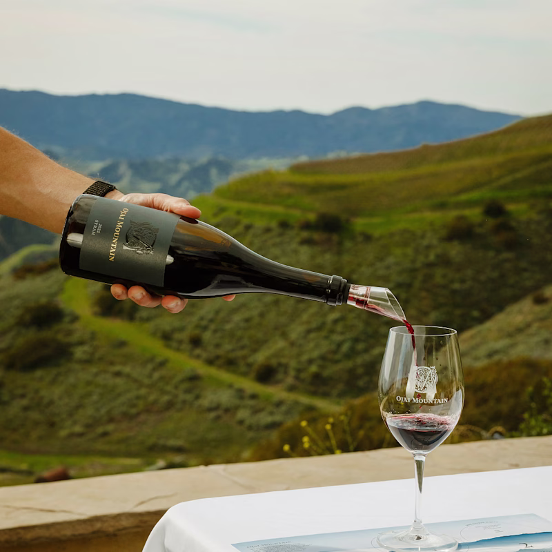 Hand pouring Ojai Mountain wine into a glass above green rolling hills