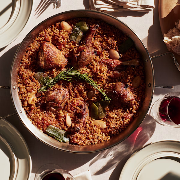 Paella Valenciana on the Table Finished Valencian paella in a steel pan on a set table with red wine alongside
