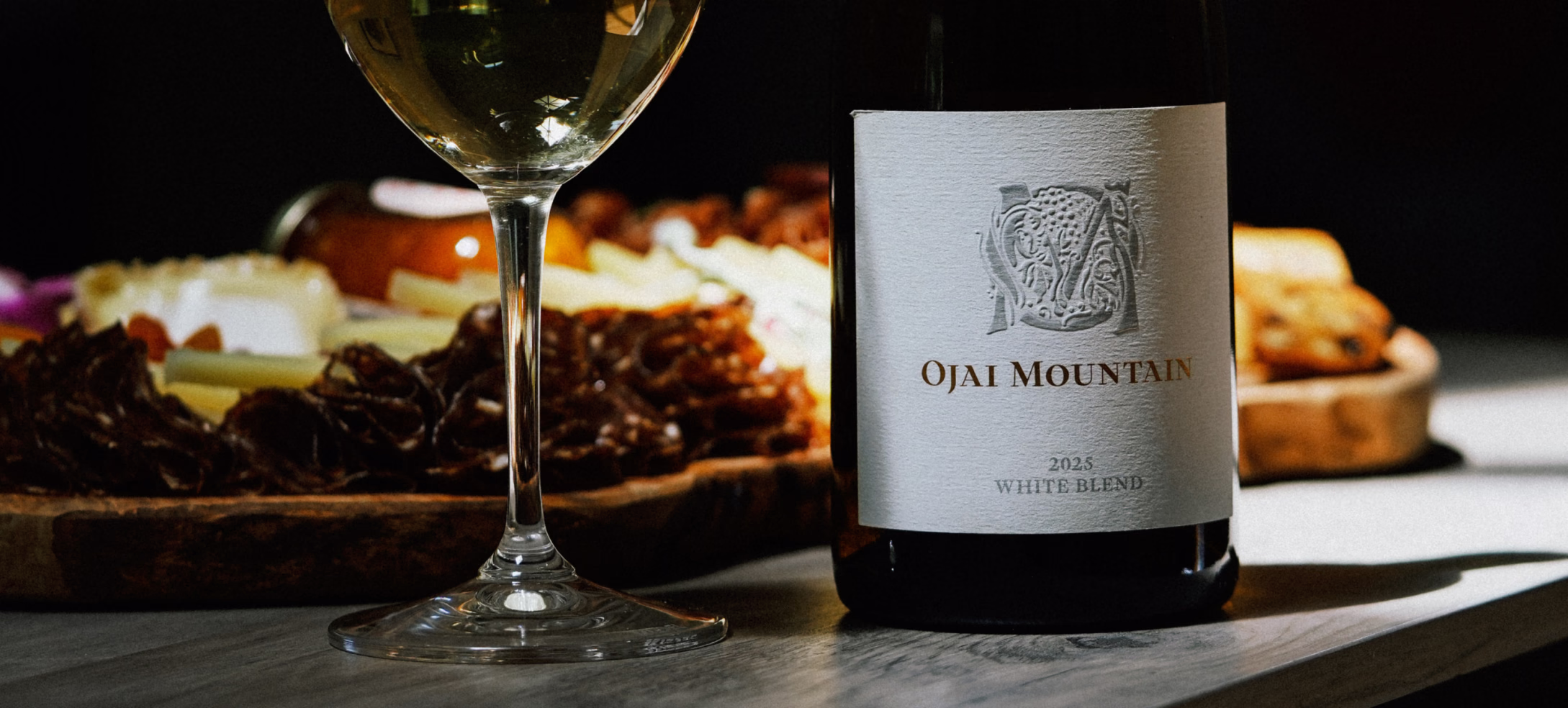 2025 White Blend with Charcuterie Ojai Mountain 2025 White Blend bottle and empty glass beside a charcuterie board