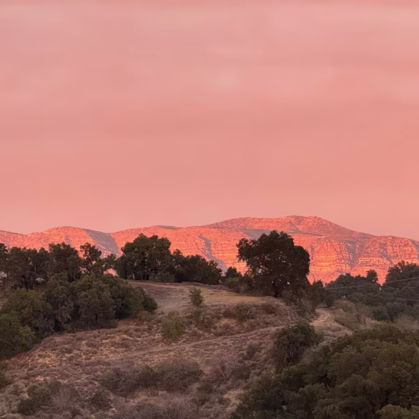 Topatopa Bluffs — Pink Moment The Topatopa Bluffs glowing pink after sunset above a dark oak-covered hillside, with a peach-coloured sky behind them