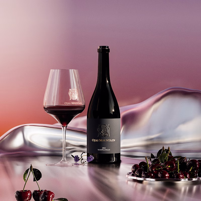 Ojai Mountain 2024 Tempranillo bottle and filled glass on silk with fresh cherries