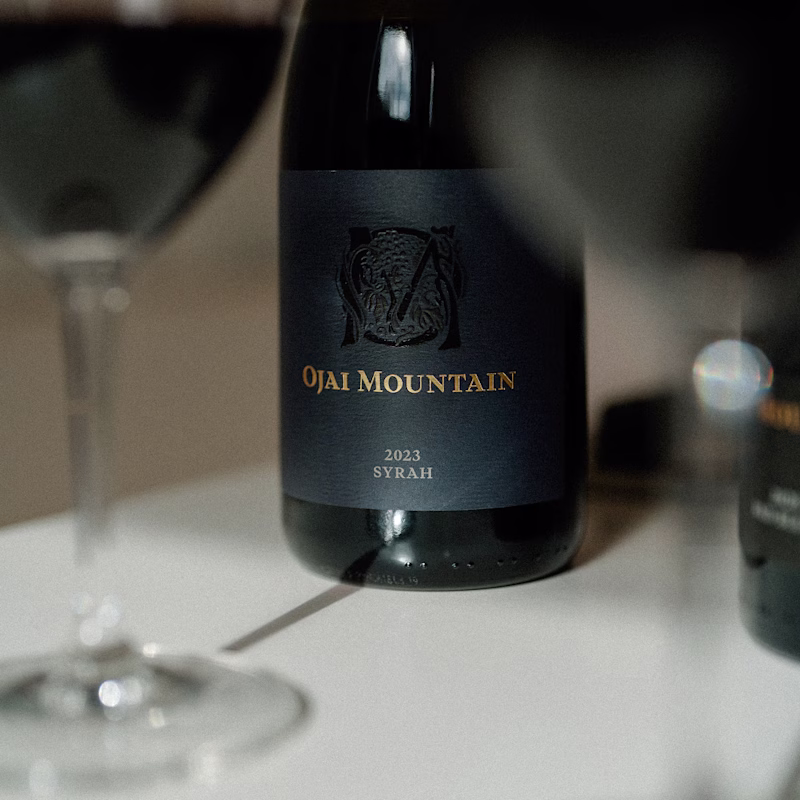 Close view of the Ojai Mountain 2023 Syrah label behind a tasting glass