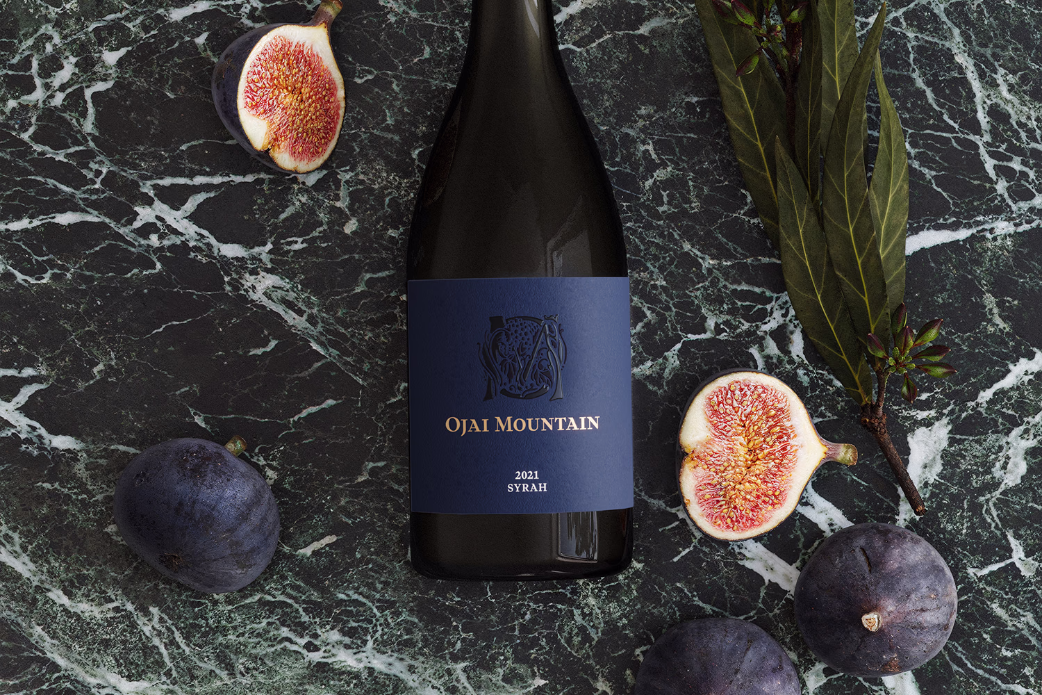 Ojai Mountain 2021 Syrah bottle on dark marble with black figs and greenery Ojai Mountain 2021 Syrah bottle on dark marble with black figs and greenery