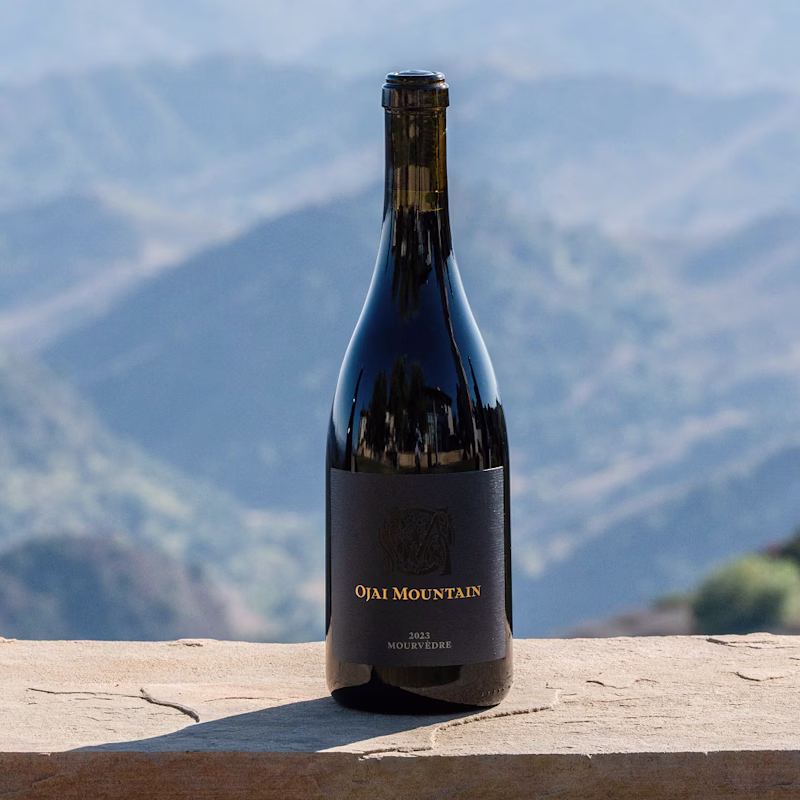 2023 Mourvèdre Gallery Image 05 Ojai Mountain 2023 Mourvèdre bottle on a stone wall above blue ridges
