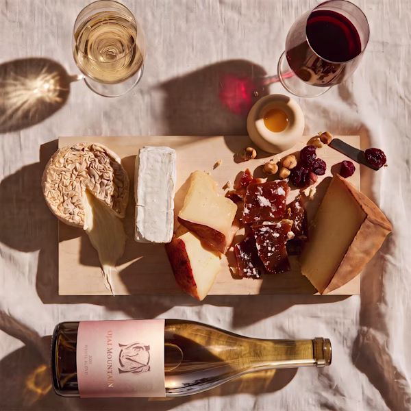 Cheese board with white and red wine and a 2025 Ojai Mountain White Blend bottle