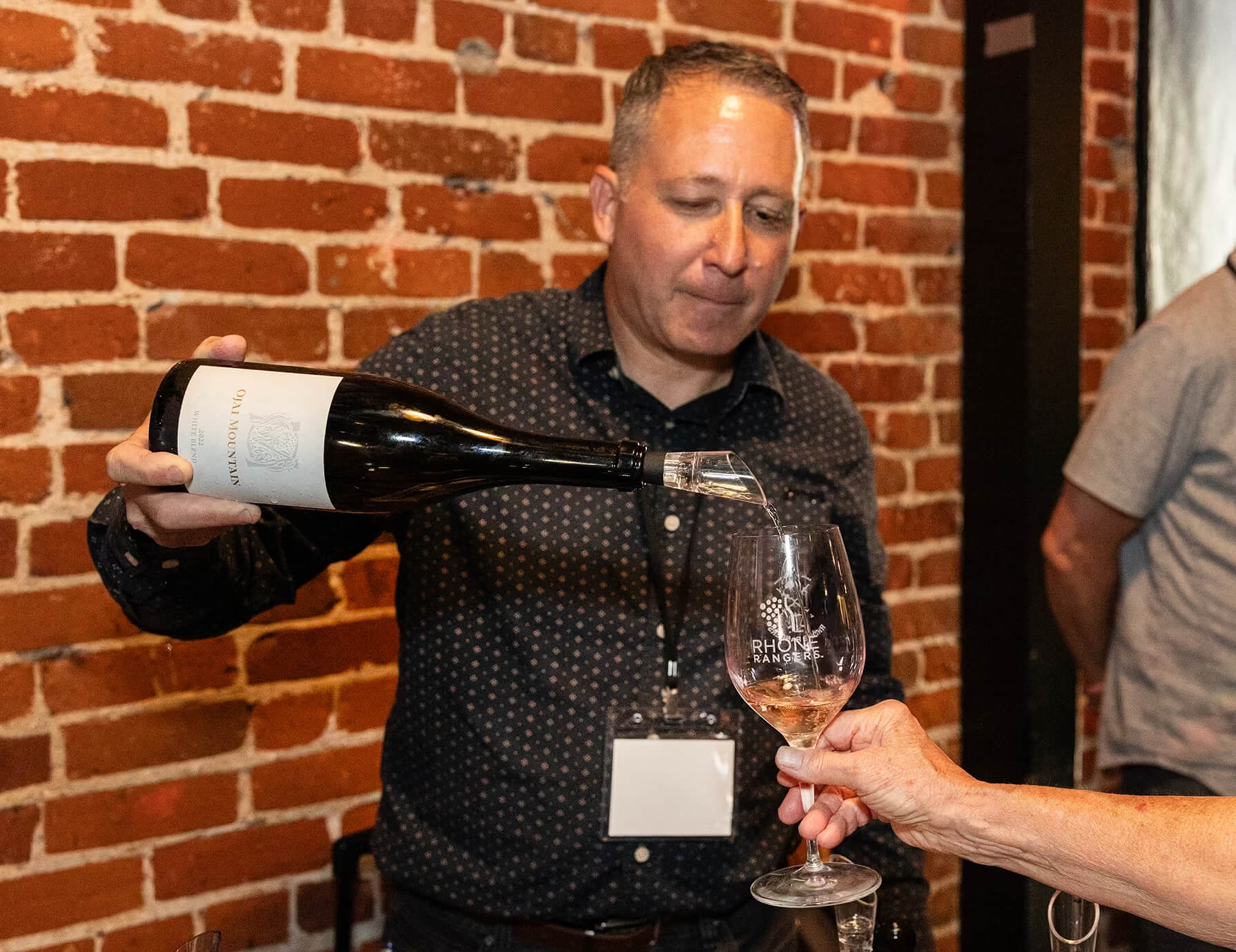 Ojai Mountain team member pouring an Ojai Mountain Estate White wine into a Rhône Rangers glass at a tasting event. Ojai Mountain team member pouring an Ojai Mountain Estate White wine into a Rhône Rangers glass at a tasting event.