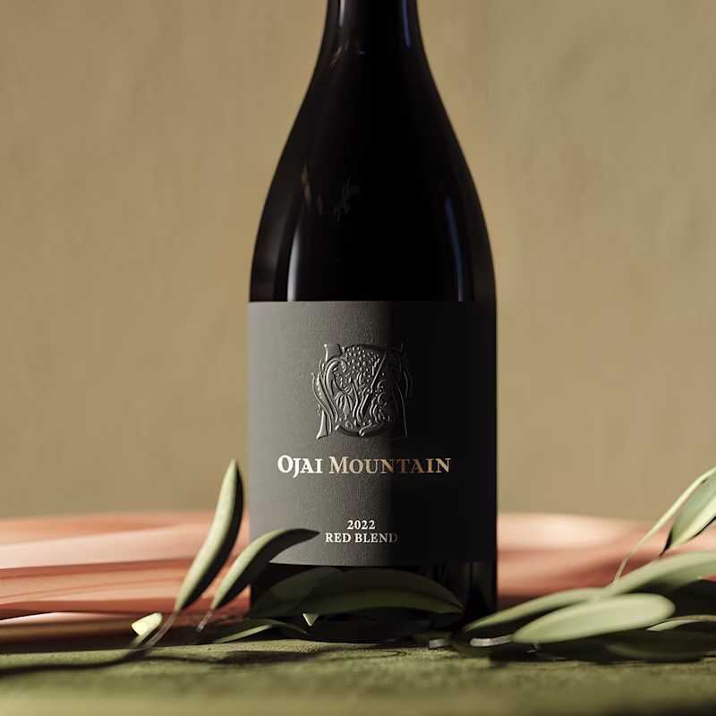 Ojai Mountain 2022 Red Blend bottle with olive branches on warm ground Ojai Mountain 2022 Red Blend bottle with olive branches on warm ground