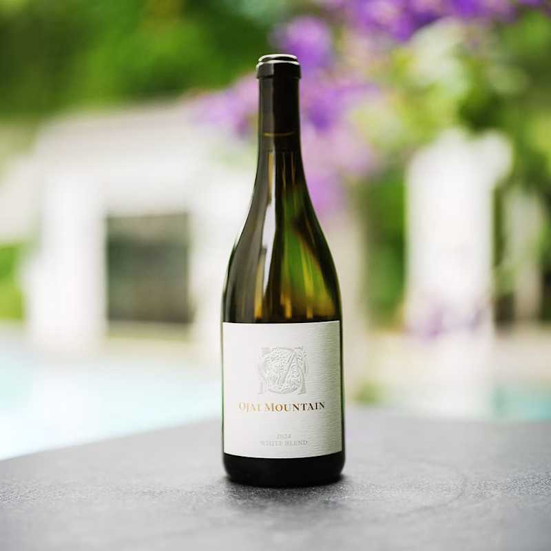 Ojai Mountain 2024 White Blend bottle on a ledge with flowers behind