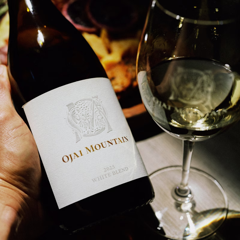 Pouring the 2025 Estate White Hand holding an Ojai Mountain Estate White bottle beside a poured glass in warm light