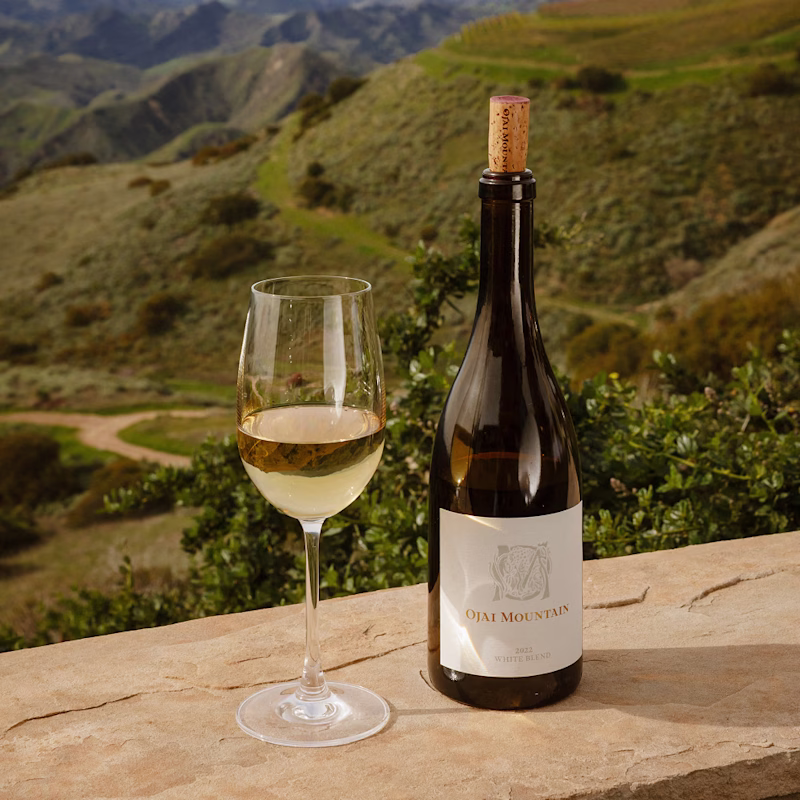 Ojai Mountain White Blend and poured glass on a ledge above green hills