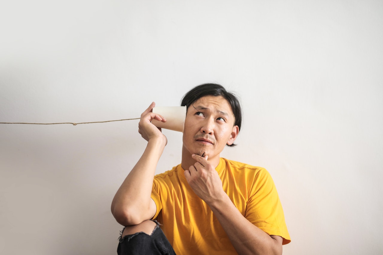 man in yellow t-shirt looks thoughtful whilst listening to paper cup phone