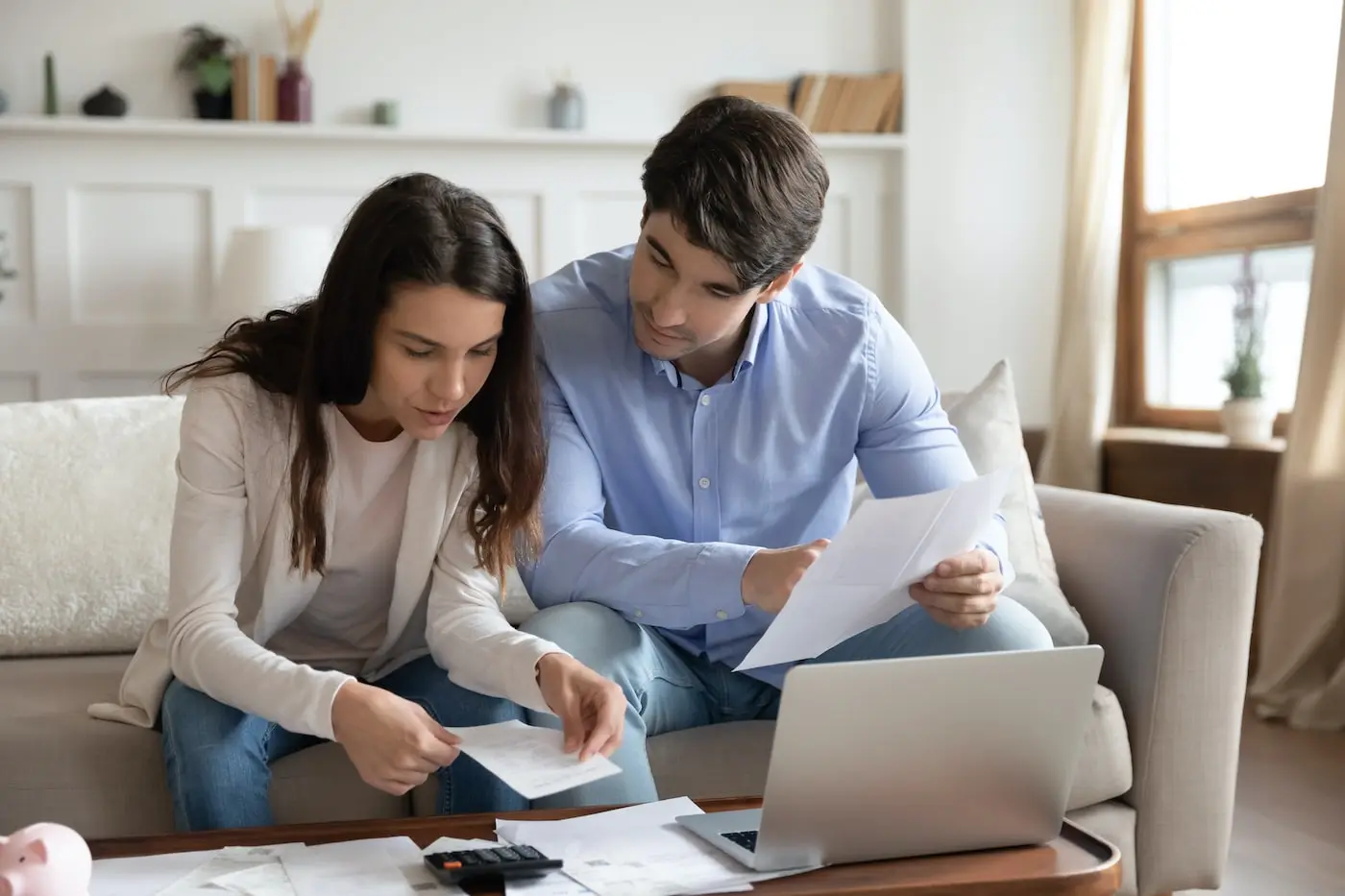 Couple sitting on a sofa reviewing property paperwork together with a laptop and calculator