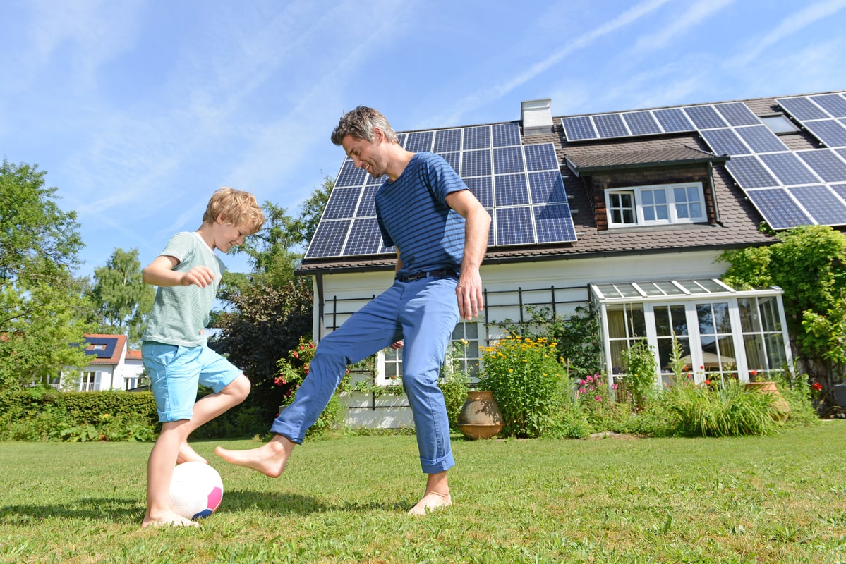 father and son playing football outside a house with solar panels