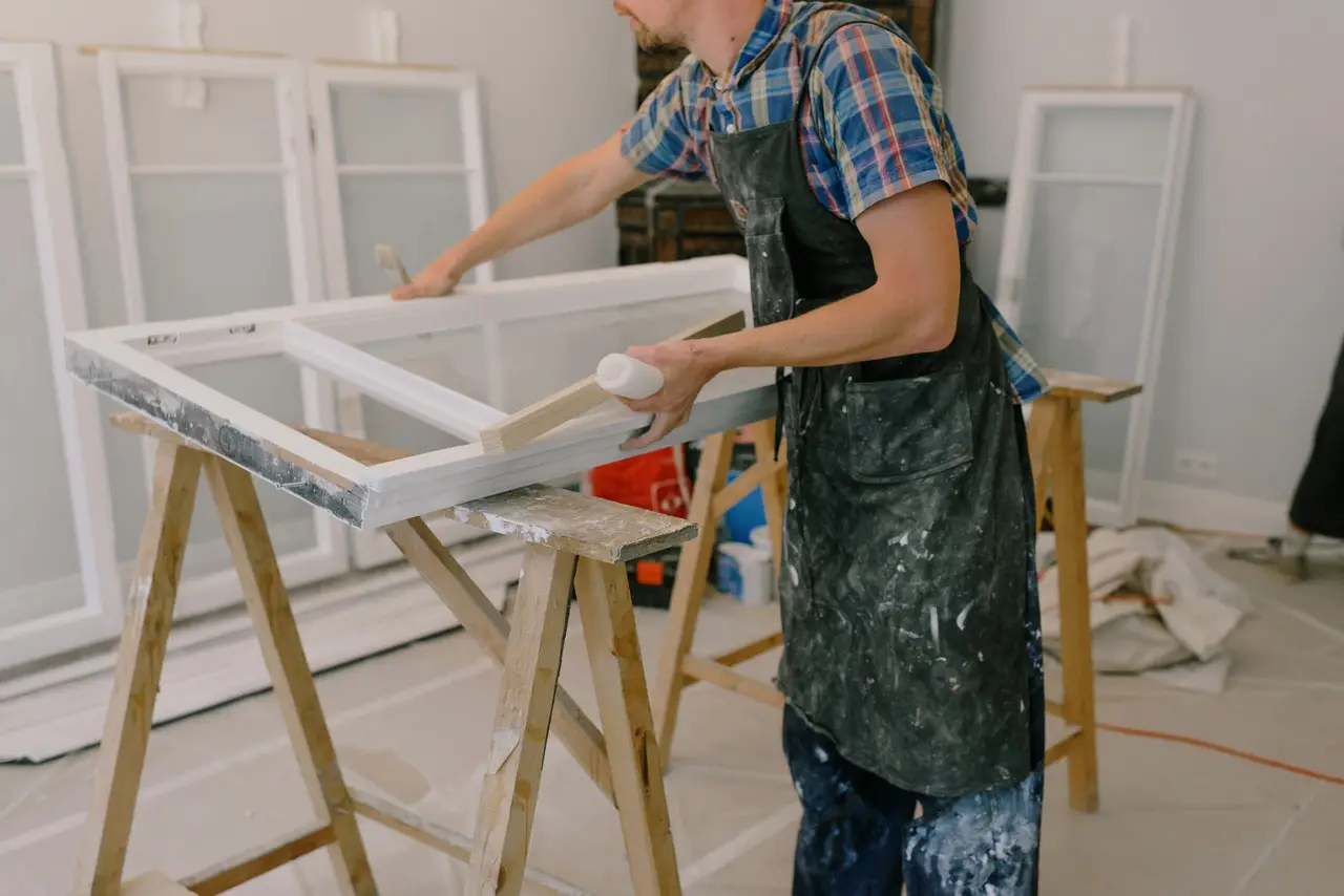 A tradesperson preparing a window frame during a home renovation, illustrating the finishing work involved in a garage conversion.