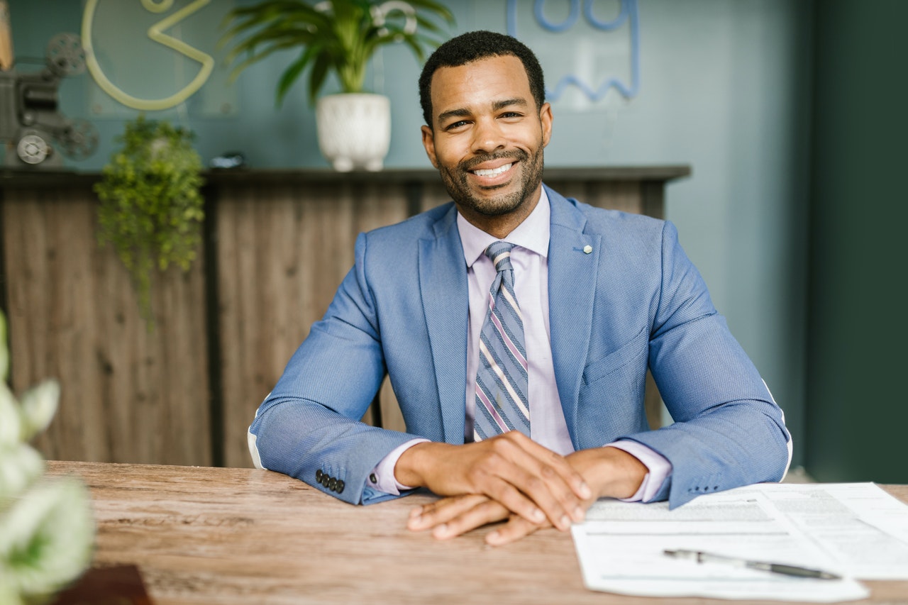 Man in blue suit smiling and sitting in a chair.