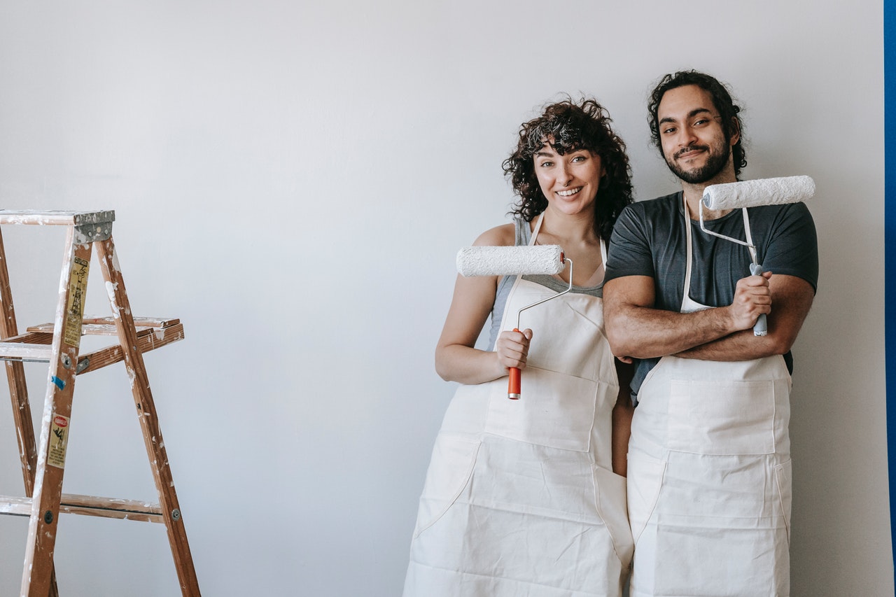 a couple pose with paint rollers and a ladder after painting the wall of their new build flat 