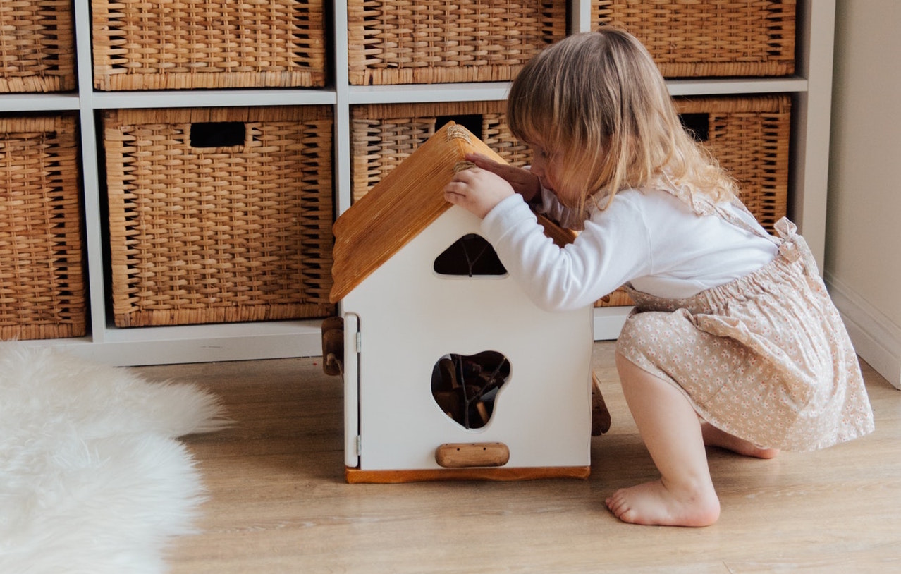 A toddler plays with a toy house made of wood 