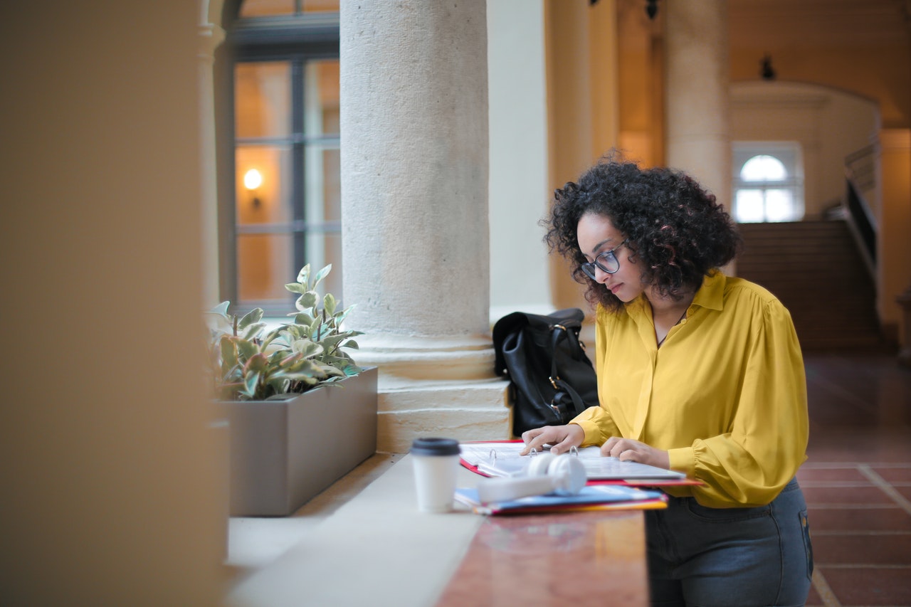 Person in yellow shirt, stood in open courtyard, studies files