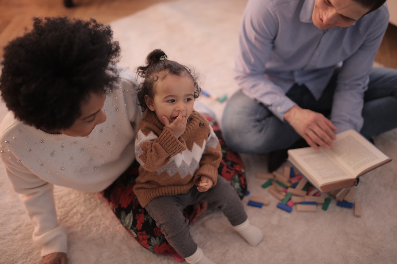 A couple reading to a young child sat on mother's knee 