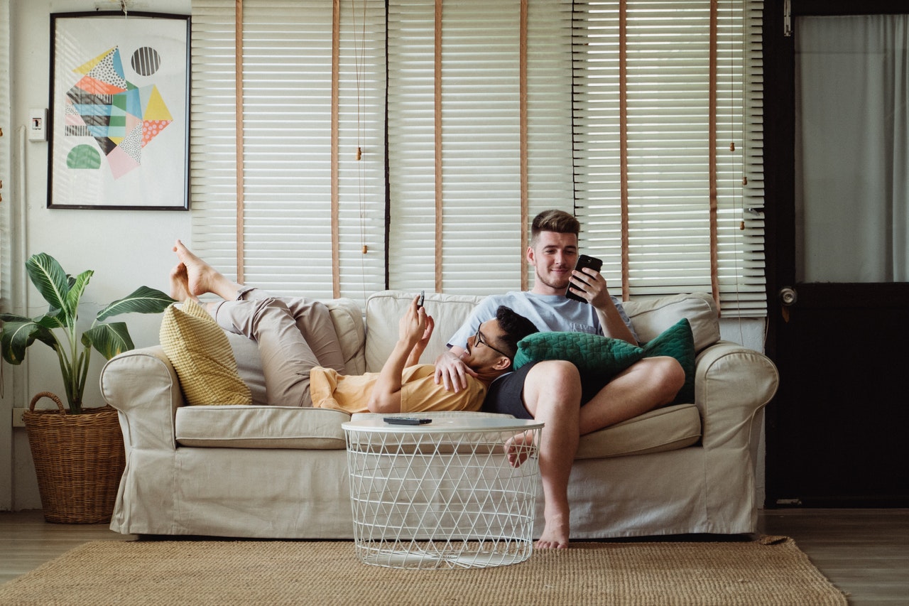 Two men relax together on a comfortable sofa, they play on their phones