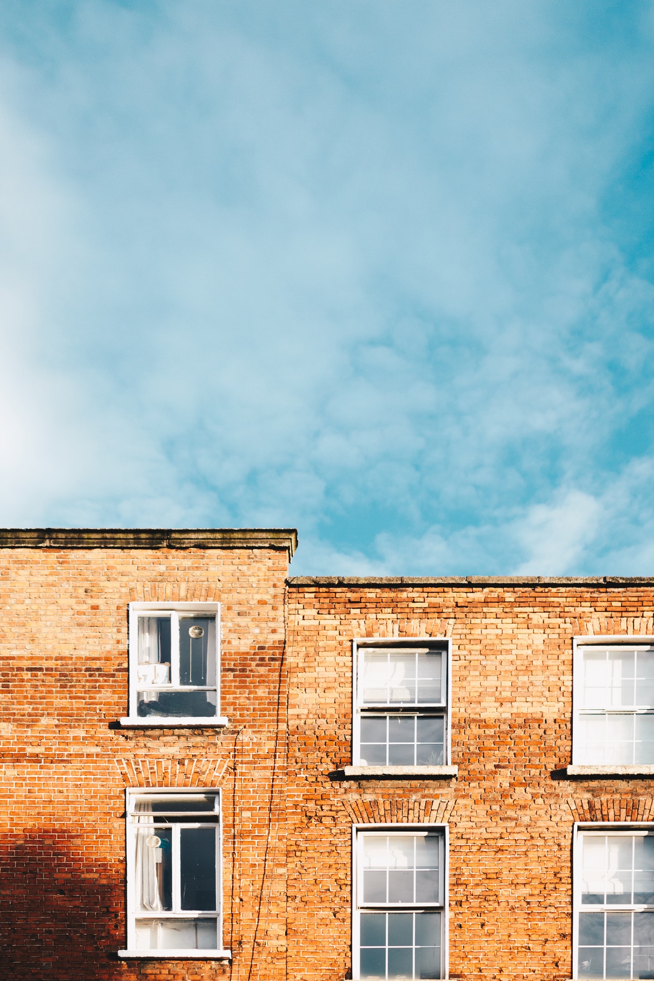 Two brick buildings joined together, one lower than the other, against background of blue sky
