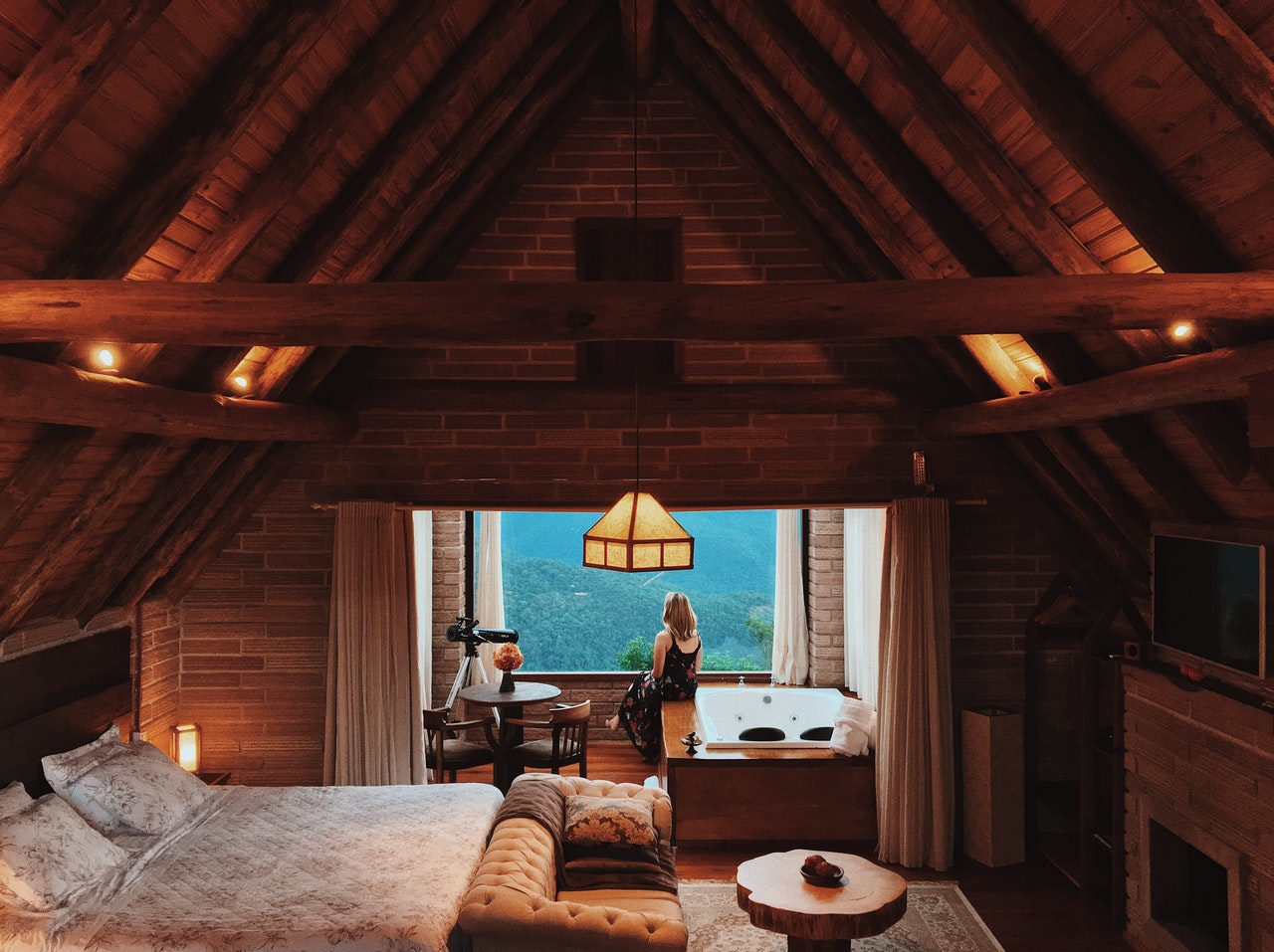 A woman standing by the window in a large attic bedroom with wooden beams