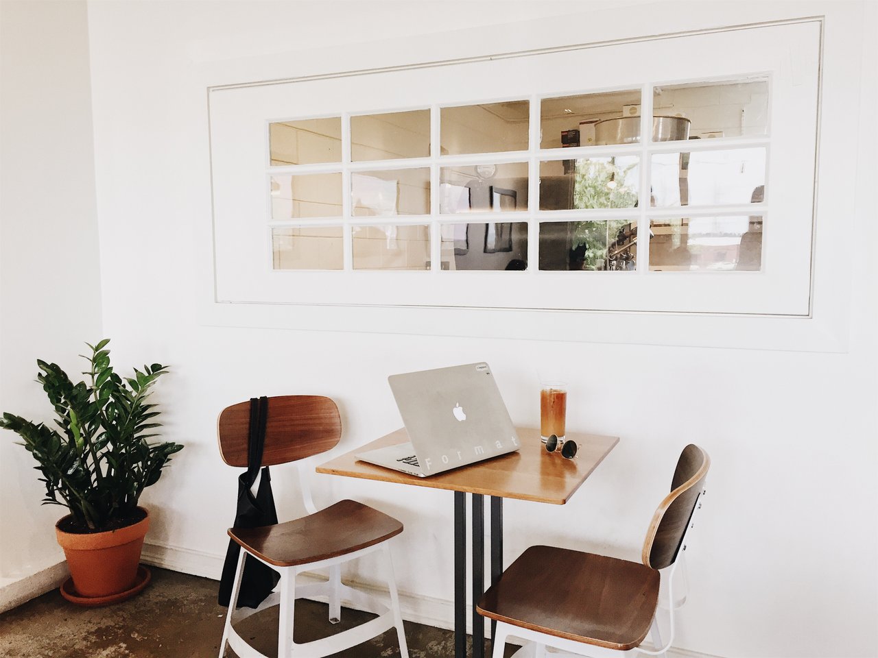A small wooden dining table and two chairs in a white minimal room with a row of windows 