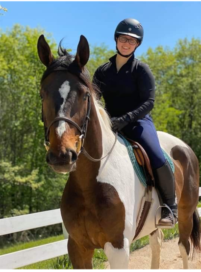 A rider in a black top and navy breeches sits on a pinto horse with a bay face and a nice stripe. 