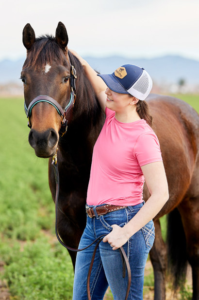 A girl standing next to a bay horse.