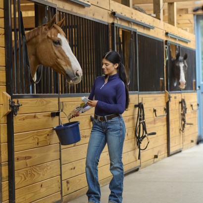 Woman putting supplements into bucket in front of horse's stall