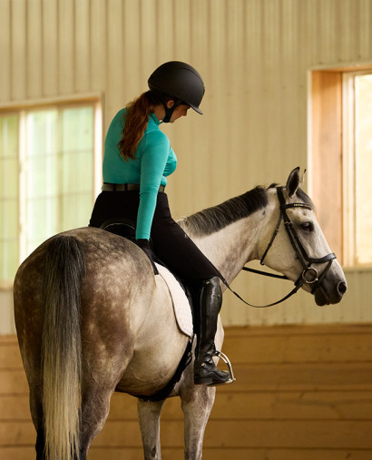 Woman on a dapple grey horse petting back behind the saddle