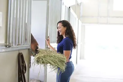 A girl giving a flake of hay to a horse