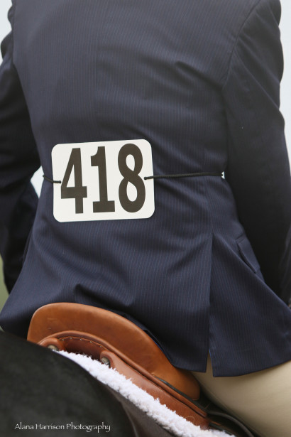 Tight shot of hunt-seat rider in navy show jacket wearing show number