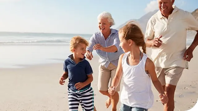 family of grandparents and children running along beach