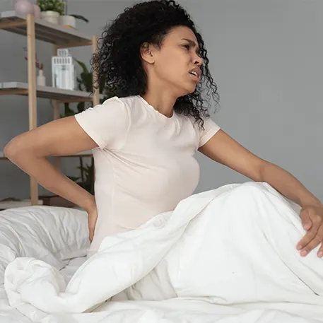 Woman sitting up in bed holding her back