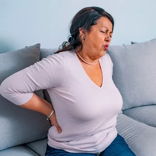  Woman holding back in pain on the sofa