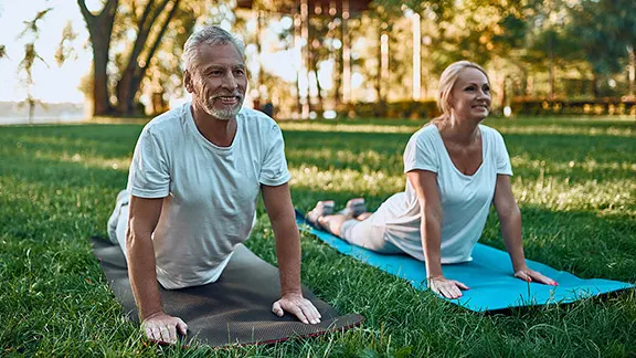 an elderly couple on yoga mats outside stretching their
