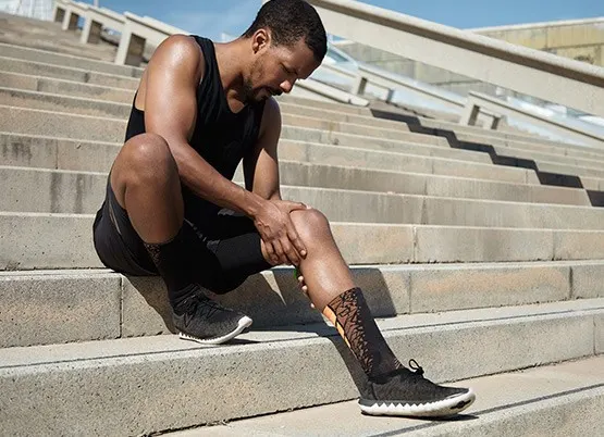 A man sitting on some steps with knee pain 